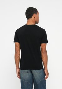 Tricou negru din bumbac cu guler rotund, mâneci scurte și o formă ajustată, expus din spate pe un fundal alb simplu.