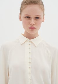 Cremefarvet bluse med klassisk krave, knap-lukning foran med matchende knapper og en blød, glat tekstur.