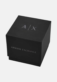 Caja cuadrada negra con "A|X" en la parte superior y "Armani Exchange" impreso en el lateral, fotografiada sobre un fondo blanco.