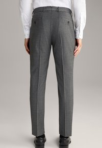 Grau karierte Hose aus gewebtem Stoff, mit flachem Frontschnitt, zwei Gesäßtaschen und taillierter Passform. Die Schuhe sind schwarz.