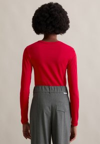 Czerwona bluzka z długim rękawem i okrągłym dekoltem, w zestawieniu z szarymi spodniami w prążki, które mają tylnią kieszeń i elastyczny pas.