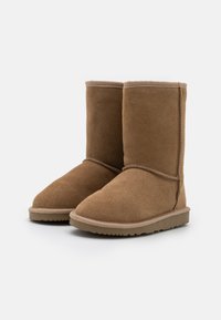 Bottines en nubuck marron avec une texture douce ; bout arrondi, coutures surpiquées et semelle en caoutchouc avec une surface texturée pour l'adhérence.
