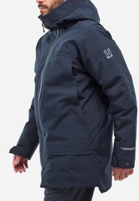 Marineblaue wasserdichte Jacke mit Reißverschluss vorne, verstellbare Kapuze, Bündchen und reflektierenden Akzenten. Glatte Textur mit einem lässigen Schnitt.