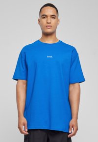 Blå bomull T-skjorte med korte ermer, med en rund hals og ordet "loved." i hvit tekst på brystet. Figursydd design.