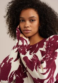 Jauka, adīta džemperis ar bordo ziedu rakstu uz krēms krāsas fona, brīva piegriezuma, ar ribotām piedurknēm. Mīksta tekstūra un plašas piedurknes.