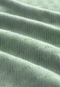 Világoszöld textil, puha, textúrált mintával, amely finom geometriai alakzatokat és vonalakat tartalmaz, réteges hatást keltve.