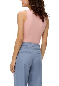 Rosa tailliertes Trägershirt mit Rundhalsausschnitt, kombiniert mit hellblauen, hochtaillierten Hosen, die über zwei hintere Taschen und einen strukturierten Stoff verfügen.