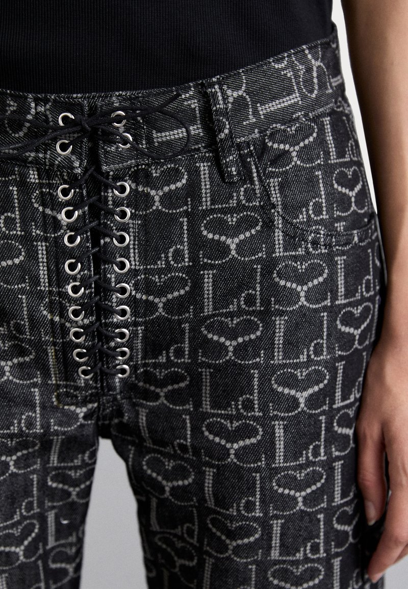 Svarta denimbyxor med snörning framtill och metalliska ögla detaljer samt ett upprepande logomönster i grått. Strukturerad tyg med en figurnära design.