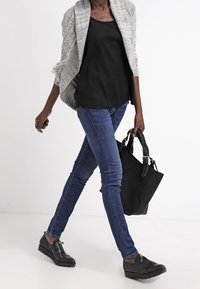 Svart linne, grå öppenstickad kofta, blå slim fit-jeans, svarta texturerade skor och en svart handväska med axelrem. Avslappnad outfit.