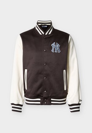 Svart-hvit varsityjakke med trykknapper, stripete krage og mansjetter, sidelommer og New York Yankees-logo på brystet.