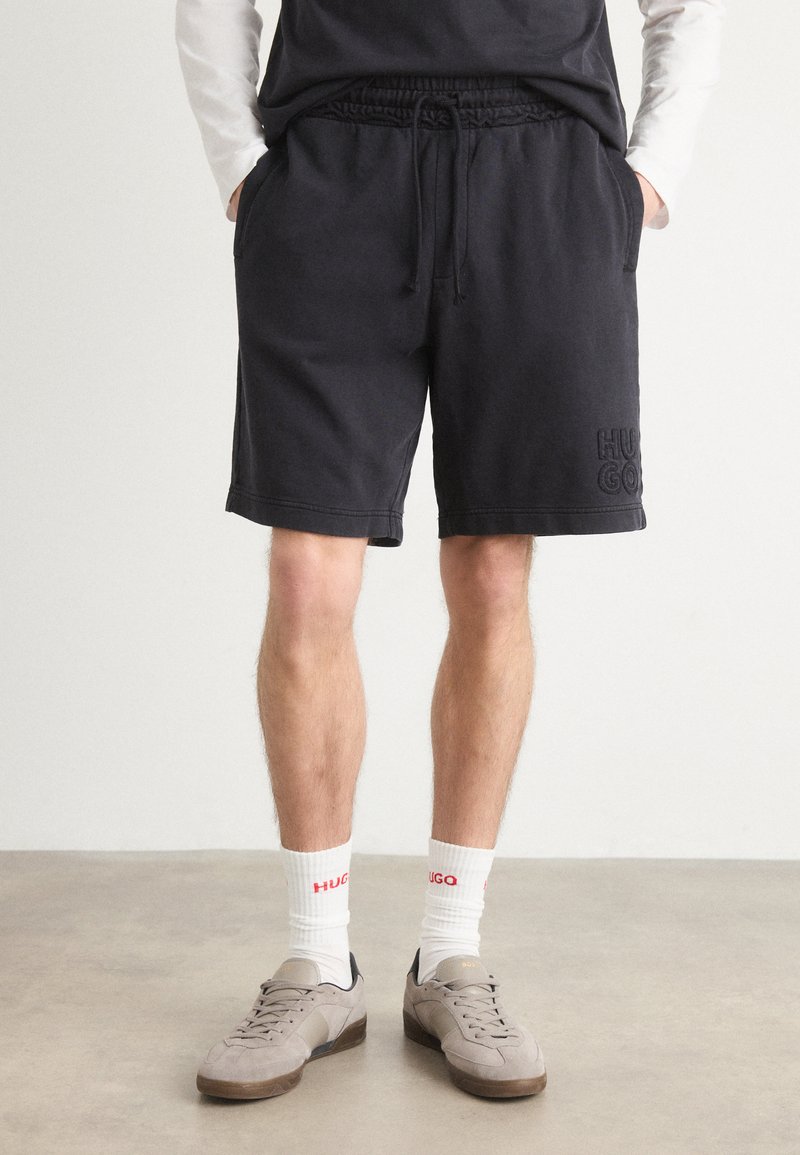 Sorte bomuldsblandede shorts med elastisk talje, sidelommer og broderet "HUGO" logo på venstre ben. Flade syninger ved kanten.