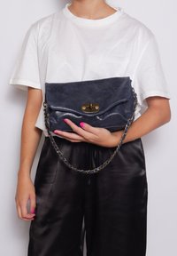 Borsa a pochette in pelle blu navy con tracolla a catena, texture leggermente spiegazzata, patta frontale e dettaglio della chiusura in tonalità oro, tenuta contro uno sfondo semplice.