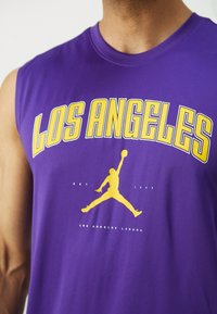 Cămașă fără mâneci de culoare mov, cu textul "LOS ANGELES" în font galben, prezentând o siluetă galbenă a unui jucător de baschet și textul "LOS ANGELES LAKERS".