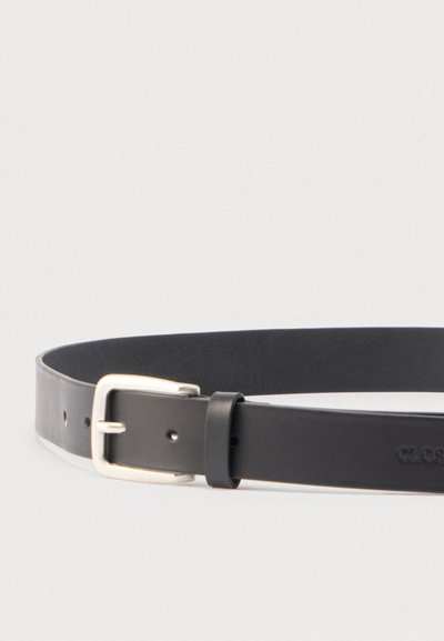 Μαύρη δερμάτινη ζώνη με ασημένια μεταλλική αγκράφα και ραμμένο θηλάκι ζώνης σε απλό ανοιχτό φόντο.