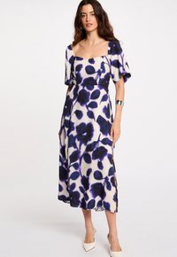 Robe midi florale en crème avec des motifs bleu foncé et violet, décolleté carré, manches courtes bouffantes et fentes latérales. Texture de tissu lisse.