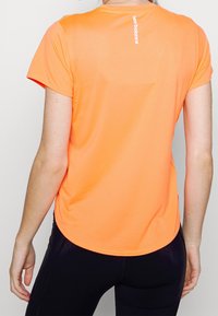 Camiseta deportiva de color naranja brillante con mangas cortas, textura acanalada, dobladillo redondeado y pequeño logotipo blanco en la parte posterior del cuello.