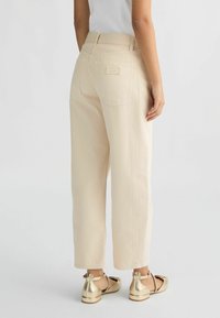 Pantalones de algodón de talle alto beige, con patas rectas y bolsillos traseros. Combinados con bailarinas metálicas doradas.