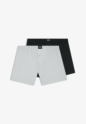 Twee paar boxershorts, één lichtgrijs met knoopvliezen en één zwart, beide met elastische taillebanden en BOSS-labels.