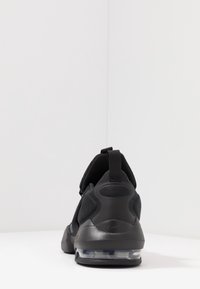 Zapatilla deportiva negra con suela de goma lisa, collar acolchado, parte superior de malla y una pestaña trasera para facilitar su colocación. Amortiguación de aire clara visible.