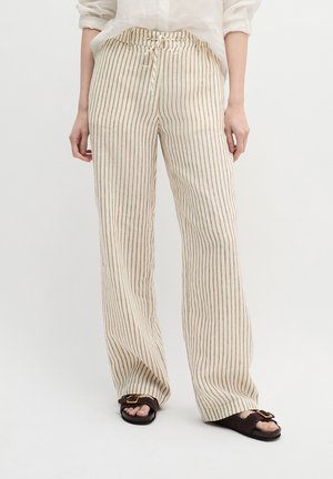 Beige-weiße, vertikal gestreifte Leinenhose mit Kordelzug in der Taille, getragen mit braunen Sandalen und einem in die Hose gesteckten weißen Hemd.