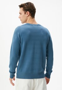 Blauer Strickpullover mit strukturierter Oberfläche, Rundhalsausschnitt, gerippten Bündchen und Saum sowie lockerer Passform. Sichtbare Nähedetails auf der Rückseite.