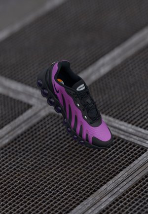 Violet ir juodas Nike Air Max sportbaigis su unikaliu suapvalintu oro pagalvės padu, pateiktas metalinės grotelės fone.