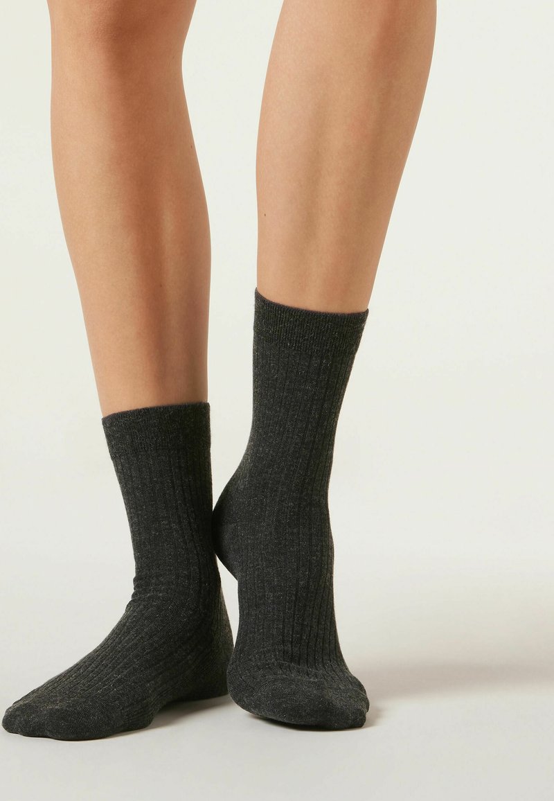 Graue gerippte Socken mit einem Bündchen-Design, hergestellt aus einem strukturierten Strickmaterial, das den Knöchel und einen Teil der Wade bedeckt.
