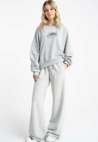 Jasnoszara bluza z oversize'owymi rękawami i grafiką na przodzie, zestawiona z dopasowanymi szerokimi spodniami dresowymi z miękkiego materiału.