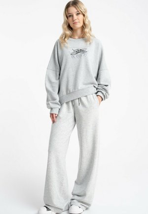 Jasnoszara bluza z oversize'owymi rękawami i grafiką na przodzie, zestawiona z dopasowanymi szerokimi spodniami dresowymi z miękkiego materiału.