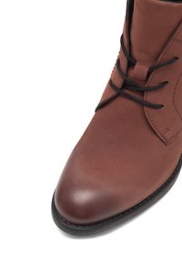 Botine din piele maro, cu vârf rotunjit, șireturi negre, textură netedă și detalii cusute pe partea superioară. Talpă din cauciuc.