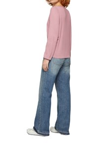 Getailleerde roze gebreide trui met lange mouwen, gecombineerd met hoge taille wijdvallende blauwe jeans en witte sneakers, met een casual stijl.