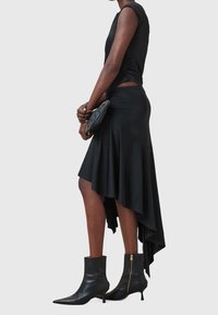 Svart asymmetrisk klänning i ett mjukt material, med en samlad midja och utsvängd nederdel. Matchad med åtsittande svarta ankelstövlar.