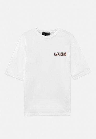 Camiseta de algodón blanca de manga corta y escote redondo, con un logo impreso en marrón en el lado izquierdo del pecho que indica el 30 aniversario.