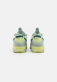 Jasnozielone buty sportowe z siatkową cholewką, szarymi i niebieskimi akcentami oraz przezroczystą żółtą podeszwą z teksturowanym wzorem.