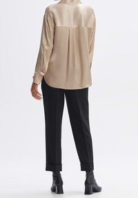 Blouse en satin beige avec un pli au dos, associée à un pantalon noir aux revers roulés, et des bottines noires à talons. Texture lisse dans l'ensemble.