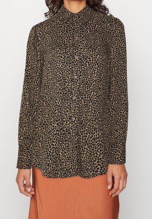 Kvinde iført en langærmet skjorte med sort og brun leopardmønster, kombineret med et rustfarvet skørt.