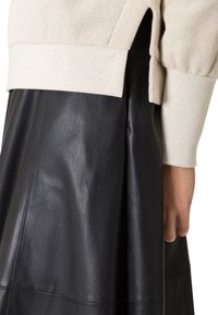 Asymmetrische top in beige breiwerk met aansluitende manchetten, gecombineerd met een zwarte leren rok met een soepele textuur en gestructureerde naden.