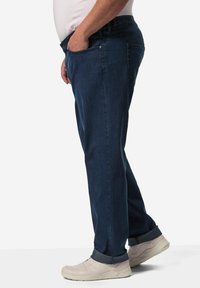 Dunkelblaue Jeans im entspannten Schnitt, mit einem traditionellen Fünf-Taschen-Design und umgeschlagenen Säumen. Kombiniert mit beigen Sneakers.