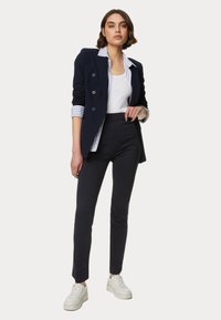 Námořnický dvouřadý blazer přes bílý top na ramínka, v kombinaci s elegantními námořnickými kalhotami a bílými teniskami; pruhované manžety a slim fit design.