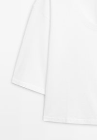 Wit katoenen T-shirt met korte mouwen en een ronde hals, getoond van de borst tot halverwege de zoom tegen een witte achtergrond.