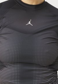 Musta urheilu-toppi, joka on valmistettu sileästä kankaasta. Siinä on pyöreä pääntie, Jordan-logo sekä pilkullinen kuvio, jossa on harmaasta mustaan kaatuva värigradientti.