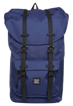 Sac à dos bleu avec sangles à boucle noire, poche avant avec fermeture éclair et étiquette "Herschel Supply Company" sur le rabat de la poche.