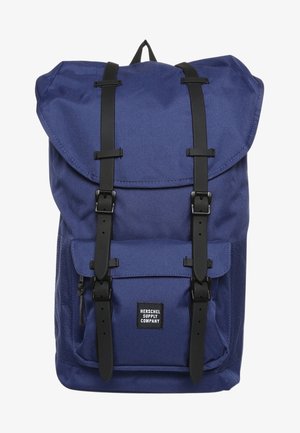 Sac à dos bleu avec sangles à boucle noire, poche avant avec fermeture éclair et étiquette "Herschel Supply Company" sur le rabat de la poche.