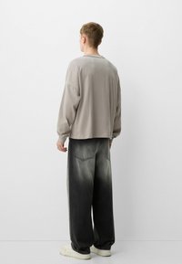 Světle šedý zkrácený svetr s dlouhými rukávy, spárovaný s vybledlými černými kalhotami se širokými nohavicemi, které mají gradaci a zadní kapsy.