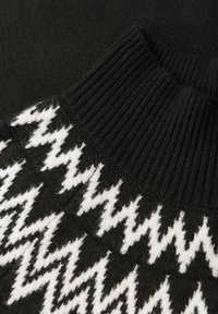 Czarny sweter wykonany z dzianiny z wysokim mówiącym kołnierzem i białym wzorem w zygzak z przodu, o miękkiej teksturze.