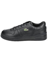Black leather sneaker with perforated design, thick sole, black laces, and a green embroidered crocodile logo. Textured accents on sides.