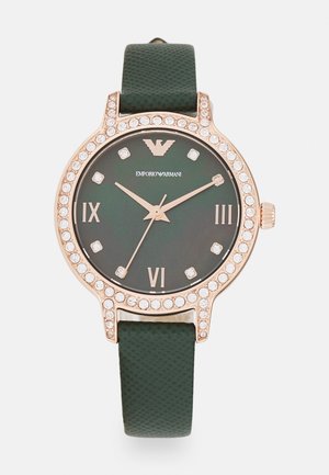 Orologio con cinturino in silicone verde, lunetta in oro rosa, dettagli in cristallo e quadrante verde scuro con numeri romani e logo.