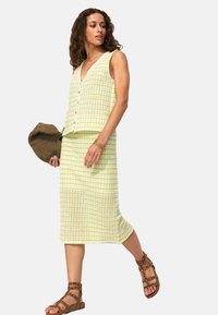 Ensemble en tricot deux pièces de couleur jaune clair et blanc, comprenant un haut sans manches et une jupe midi à rayures horizontales. Sandales à lanières marron.