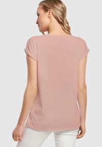 Lyserød t-shirt lavet af blødt stof, med en afslappet pasform, korte opsmøgede ærmer og en rund halsudskæring, vist fra bagsiden.