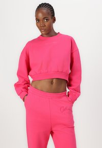 Rosa kortermet genser med lange ermer, med ribbestrikket finish og brodert logo. Matcher med joggebukser og elastisk liv.
